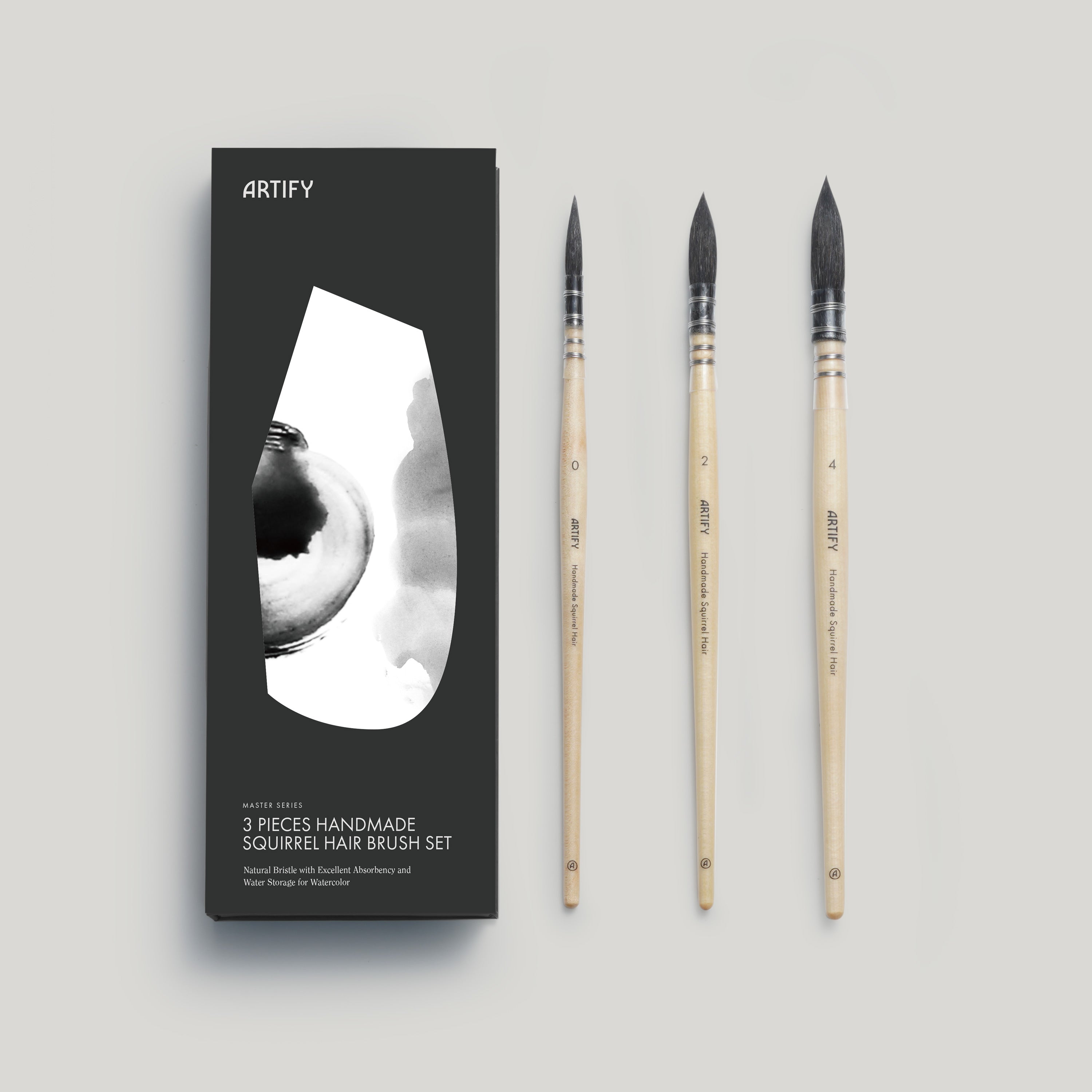 A set of three premium squirrel hair watercolor brushes by ARTIFY, displayed next to their packaging which is a sleek black box with a white brush silhouette. The brushes have wooden handles and black and white bristles, and are labeled with sizes 0, 2, and 4.