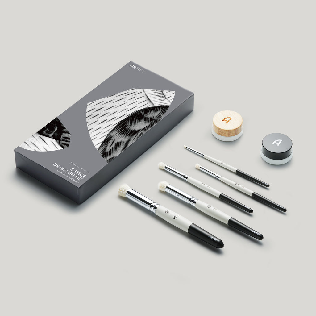 A set of high-quality drybrush brushes for miniature painting, displayed alongside their packaging which highlights a black and white design. The brushes appear to be made of high-quality goat hair with metal handles.